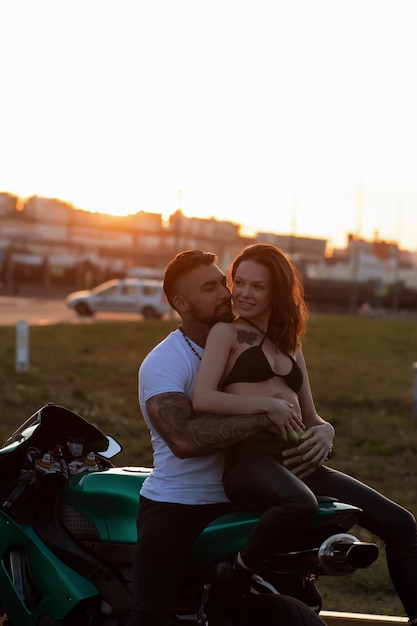 Casal abraçando perto de moto ao pôr do sol