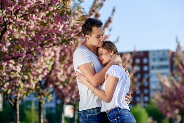 Casal abraços perto de árvores de sakura no jardim florido.