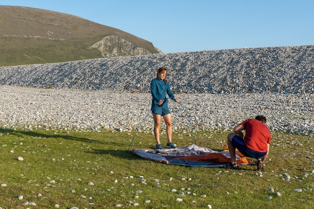 Casal acampando ao ar livre, estilo de vida, montando uma barraca em uma praia rochosa natural