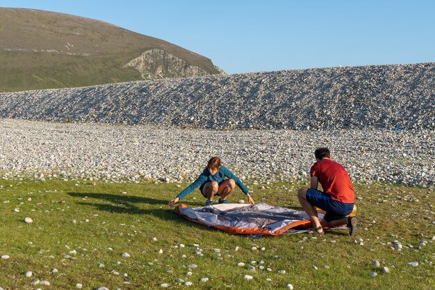 Casal acampando ao ar livre, estilo de vida, montando uma barraca em uma praia rochosa natural