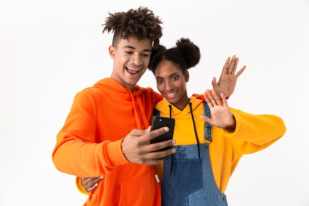 casal adolescente com roupas coloridas tirando foto de selfie no celular, isolada na parede branca