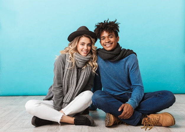 Casal adolescente feliz sentado isolado na parede azul, se abraçando