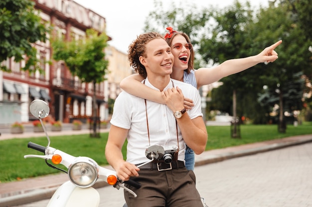 Casal adorável jovem e alegre posando junto com uma scooter retrô enquanto olha para o ar livre