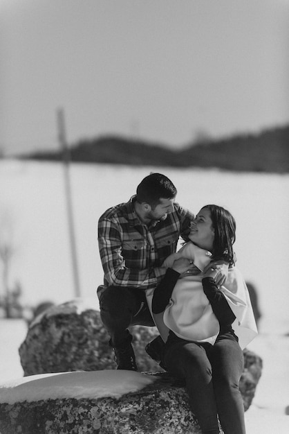 Foto casal adorável juntos nas rochas olhando um ao outro e de mãos dadas contra a vastidão nevada foco seletivo