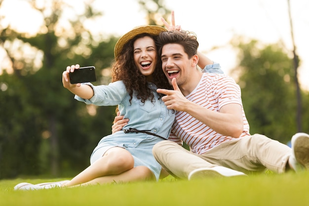 casal adorável sentado na grama verde do parque e tirando selfie no smartphone