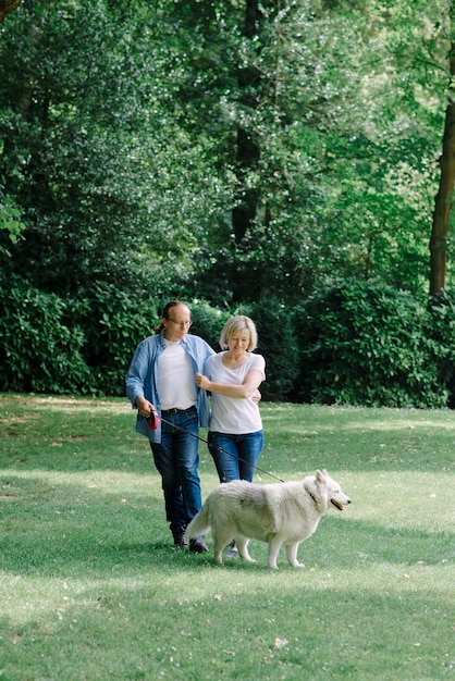 Casal adulto andando na grama com um cachorro branco