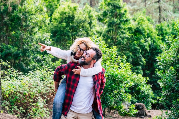 Casal adulto feliz aproveita a atividade de lazer ao ar livre da natureza junto com o homem carregando uma mulher bonita e alegre com floresta verde em cena