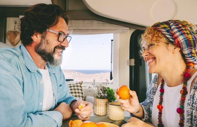 Casal adulto feliz comendo frutas juntos dentro de uma van de campista curtindo viagens férias de verão e relacionamento Homem e mulher sorrindo e se divertindo dentro da caravana com vista para a praia do lado de fora