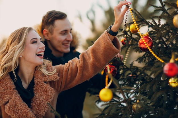 Casal adulto jovem decora a árvore de natal na floresta de abetos de madeira do parque de inverno. conceito de celebração da festa de férias de pinho de ano novo.