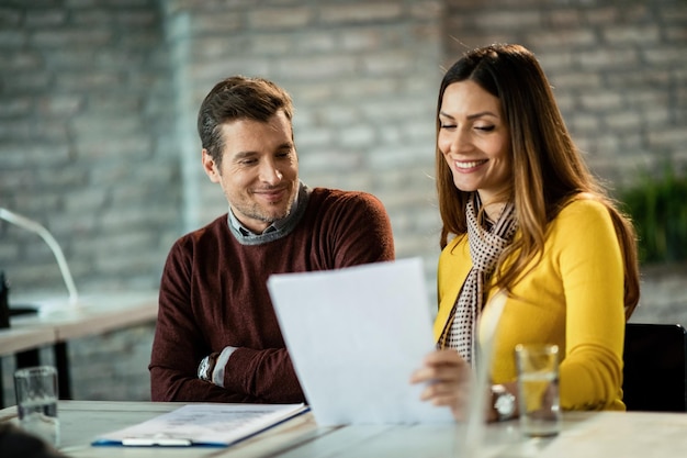 Foto casal adulto sorridente passando pela papelada e analisando seus relatórios financeiros enquanto está no escritório o foco está no homem