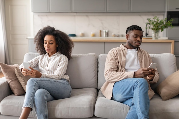 Foto casal afro-americano desapontado e entediado usando smartphones sentado em casa