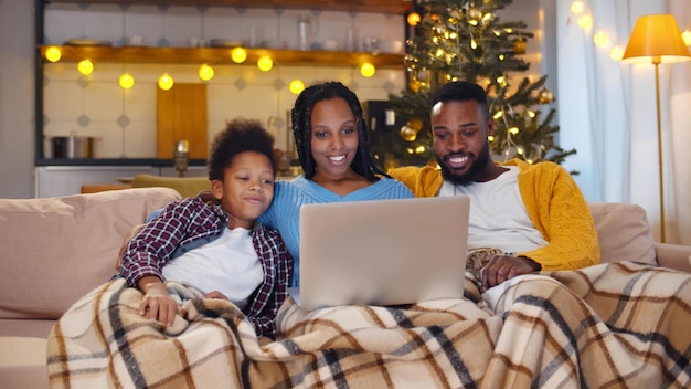 Casal afro-americano e filho sentado no sofá fazendo videochamada com a família na véspera de natal