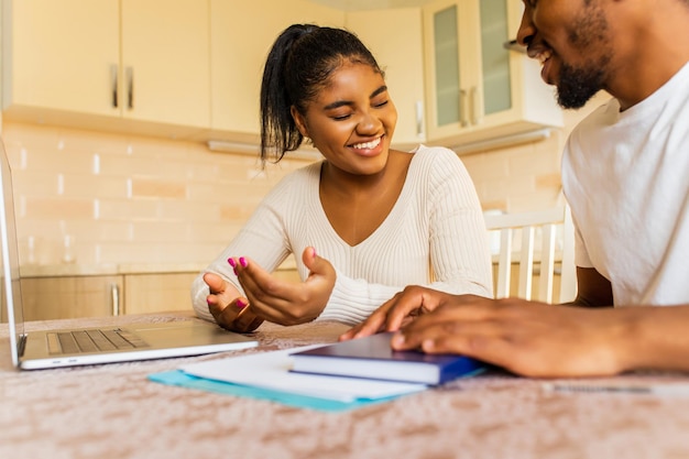 Casal afro-americano gerenciando banco de finanças e usando laptop na cozinha