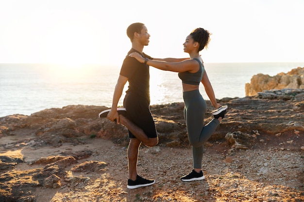 Casal afro-americano milenar positivo em roupas esportivas fazendo alongamento para pernas praticando ioga