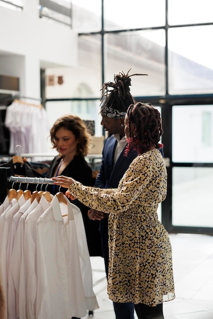 Casal afro-americano querendo comprar camisa da moda, pedindo ajuda ao funcionário do showroom durante a atividade comercial. Clientes comprando roupas casuais, comprando roupas da moda em boutique moderna