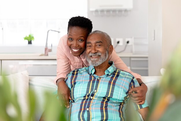 Foto casal afro-americano sênior passando um tempo em casa, abraçando, sorrindo e olhando diretamente para uma câmera. distanciamento social e auto-isolamento em quarentena.