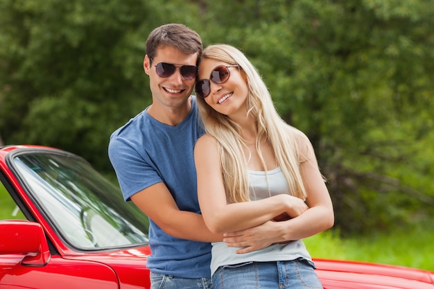 Casal alegre abraçando e encostado ao cabriolet