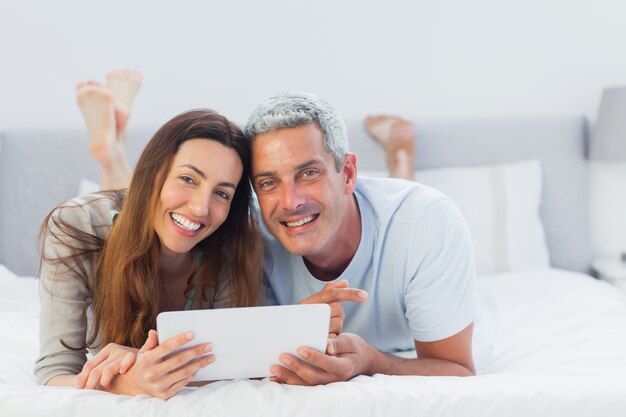 Casal alegre deitado na cama usando o seu tablet pc