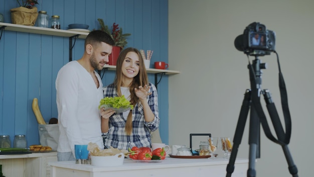 Casal alegre gravando blog de vídeo sobre comida saudável vegetariana na câmera na cozinha em casa