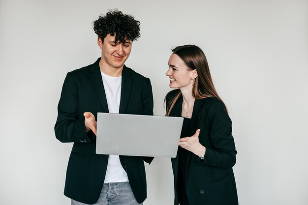 Casal alegre posando com laptop moderno e vestindo elegantes blazers pretos e acessórios para homens