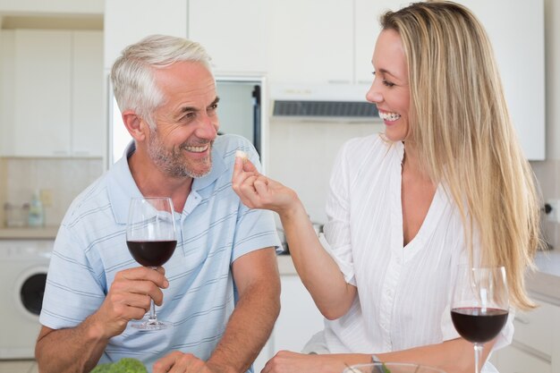 Casal alegre preparando o jantar juntos e bebendo vinho tinto