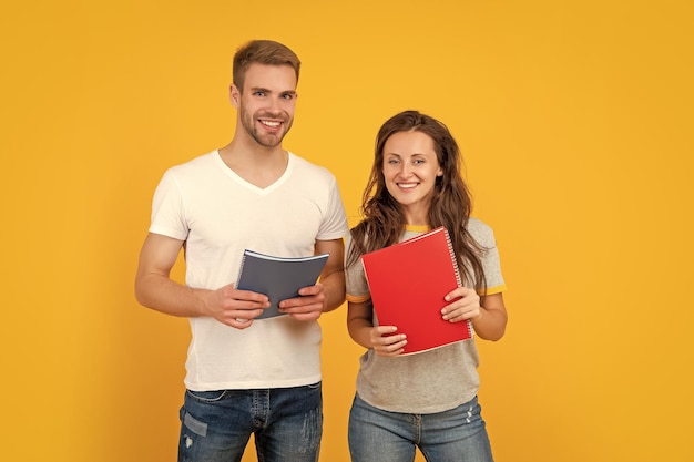 casal alegre segura o dever de casa do caderno de volta à escola educação moderna dia do conhecimento garoto e garota seguram estudantes universitários de notebook em estudo de fundo amarelo com pasta de trabalho