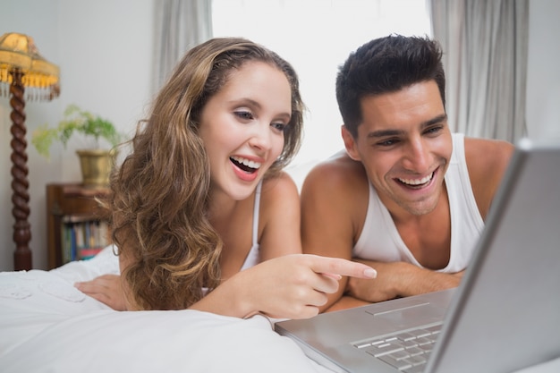 Casal alegre usando laptop na cama em casa