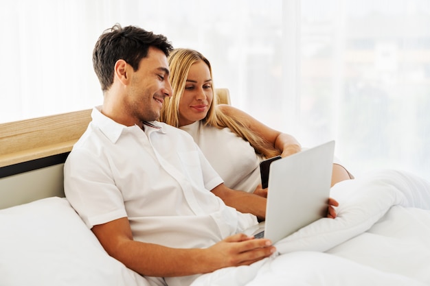 Casal amante caucasiano desfrutar com mídias sociais juntos no laptop juntos no quarto de manhã cedo