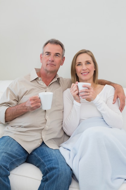 Casal amoroso relaxado com copos de café na sala de estar