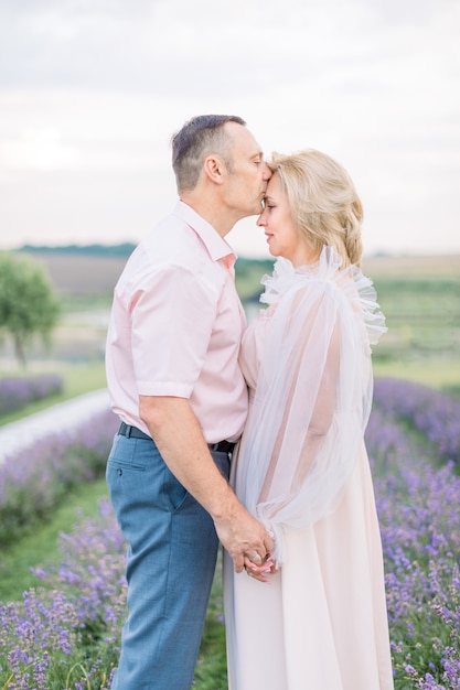 Casal amoroso romântico maduro andando no campo de lavanda. um sonho feliz caucasiano casal de meia idade na natureza, em pé de mãos dadas. homem beijando sua esposa. aproveitando o momento.