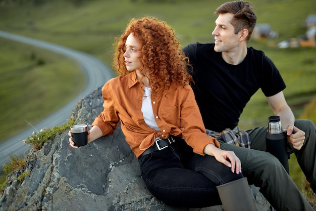 Casal amoroso sonhador sentados juntos na rocha da montanha no campo, bebendo chá