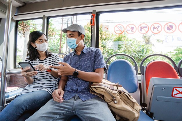 Casal andando de ônibus público usando máscara facial