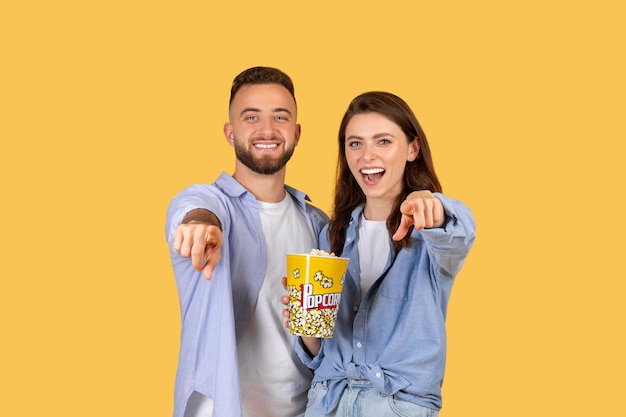 Foto casal animado apontando para a câmera com pipoca
