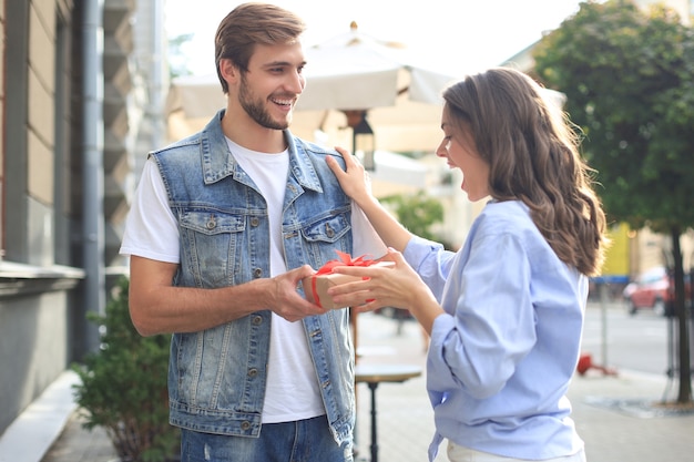 Casal animado atônito com roupas de verão, sorrindo e segurando a caixa de presente juntos em pé na rua da cidade.