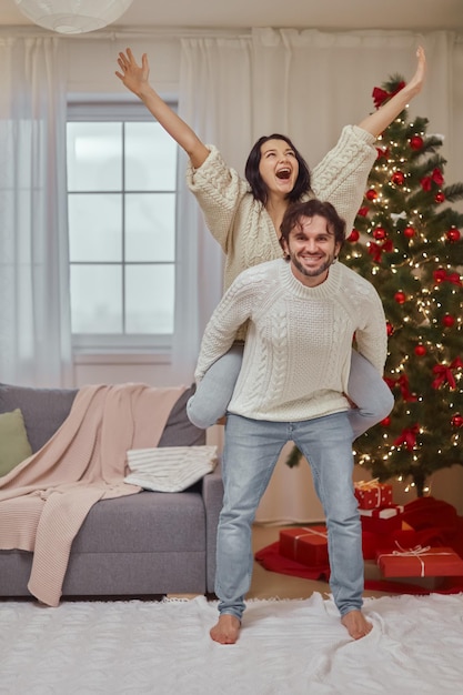 Casal animado comemorando ano novo perto da árvore de natal em casa