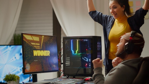 Foto casal animado gamer ganhando videogame de tiro em primeira pessoa on-line no computador poderoso rgb gritando levantando as mãos. cibercriminosos profissionais atuando durante o campeonato esport de torneio de jogos usando fones de ouvido