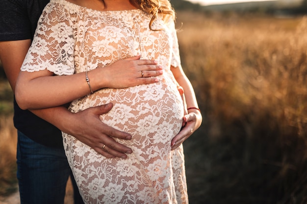 Casal ao pôr do sol com uma barriga de grávida