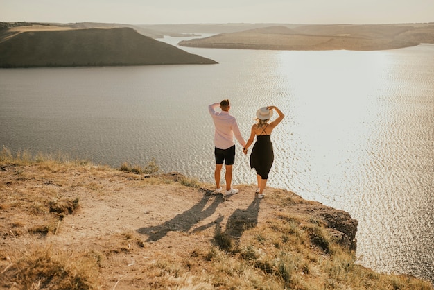 Casal apaixonado anda em uma montanha acima de um grande lago à beira-mar ao pôr do sol.