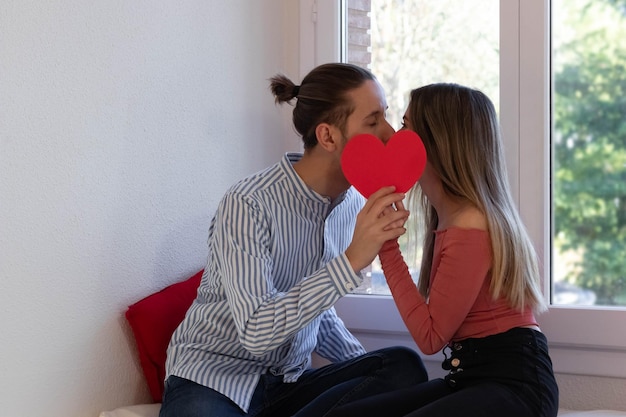 Casal apaixonado beijando atrás de um coração vermelho