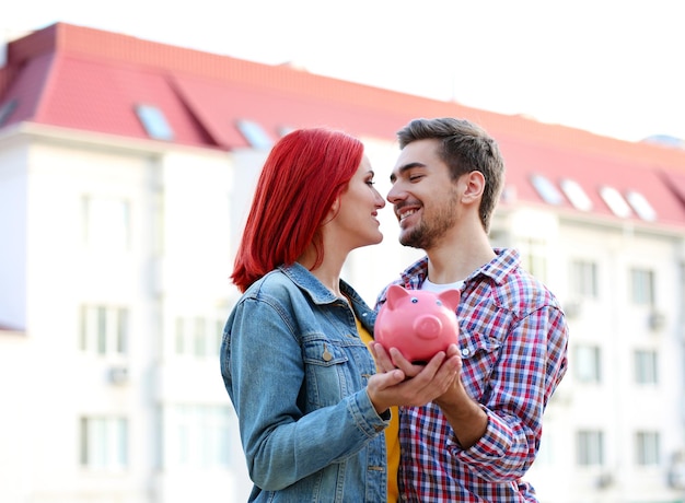 Casal apaixonado com cofrinho perto de casa de apartamento