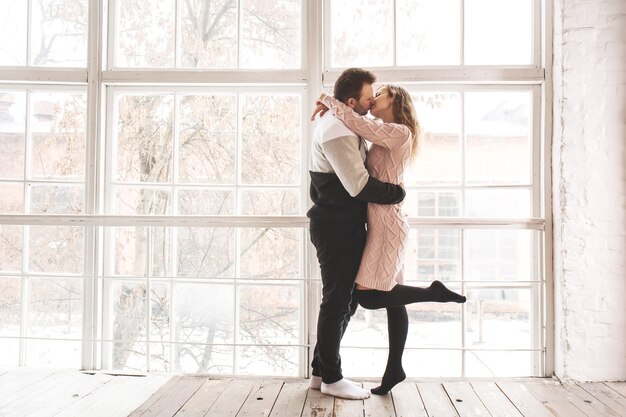 Casal apaixonado com roupas de inverno perto da janela