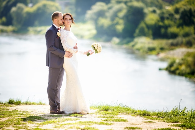 Casal apaixonado de recém-casados caminha perto do rio largo em dia ensolarado de verão