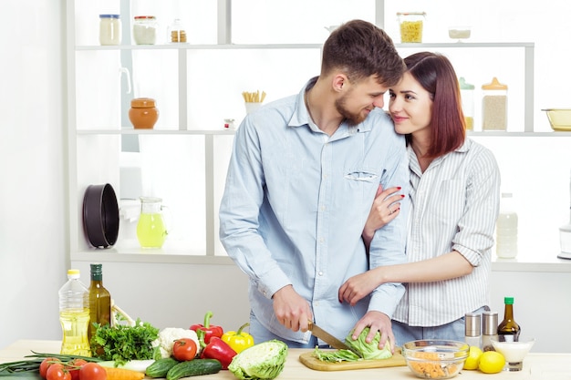 Casal apaixonado e feliz preparando uma salada saudável de legumes frescos na cozinha