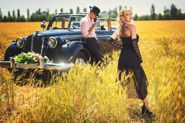 Casal apaixonado em pé perto de carro retrô no campo de trigo