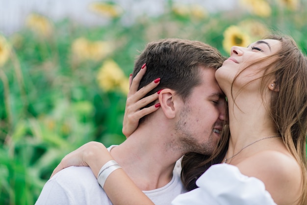 Casal apaixonado em vestidos brancos se beijando, sorrindo, rindo em um campo de girassóis