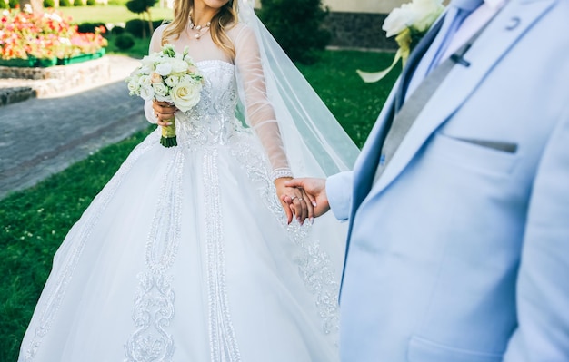 Casal apaixonado está caminhando ao ar livre Noivo de terno azul e noiva em vestido de luxo Lindo buquê nas mãos