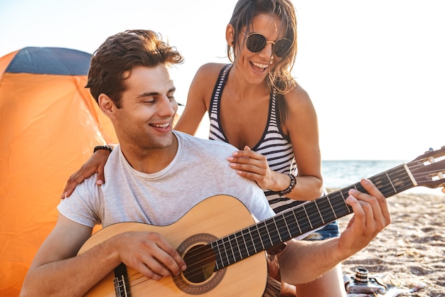 Casal apaixonado feliz e fofo tocando violão na praia ao ar livre