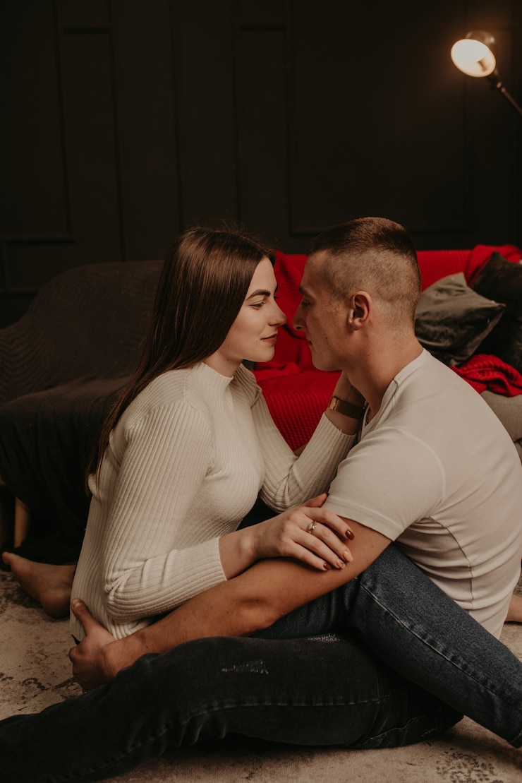 Foto casal apaixonado, homem e mulher, sentados no chão, de pernas cruzadas, se abraçando e se beijando