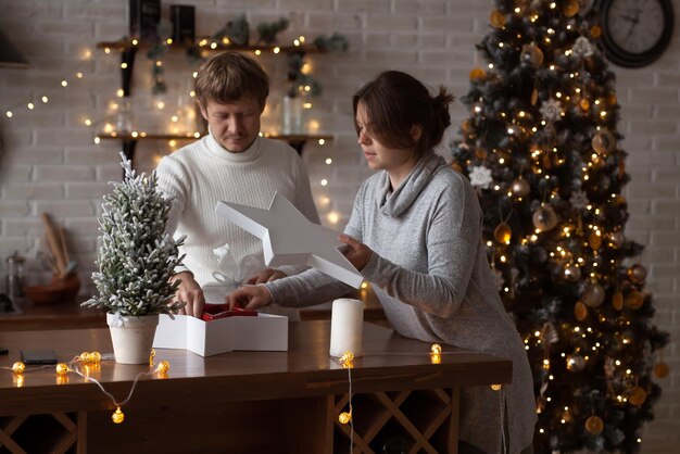 Casal apaixonado, mulher e homem desempacotando presentes em casa na cozinha decorada de Natal