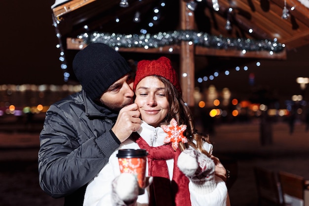 Casal apaixonado na cidade a pé bebe café com doces de Natal no inverno.